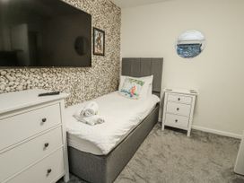 A bedroom with a bed, TV, dresser, and mirror at Daisy Cottage in Benllech