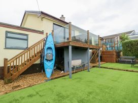 A garden with a kayak on the side and stairs leading to a deck at Daisy Cottage Benllech