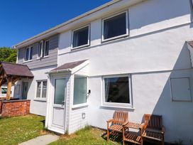 A white two-story house with wooden chairs outside on a lawn at Galwad Y Mor in Morfa Nefyn