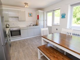 A kitchen with white cabinets and a wooden dining table with chairs and a bench at Galwad Y Mor in Morfa Nefyn
