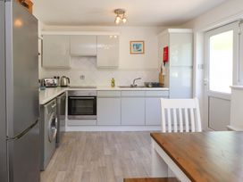 A kitchen with white cabinets and appliances including a refrigerator oven washing machine and dishwasher with a wooden dining table and white chair in Morfa Nefyn