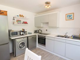A kitchen with white cabinets a washing machine dishwasher microwave and sink at Galwad Y Mor in Morfa Nefyn