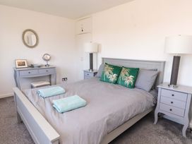 A bedroom with a gray bed, green pillows, two bedside tables with lamps, a vanity with a mirror and stool at Galwad Y Mor in Morfa Nefyn