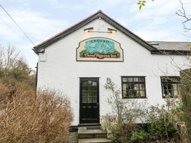 Exterior of a white building with a black door and windows with a sign reading Three Pigeons Inn above the door surrounded by bushes