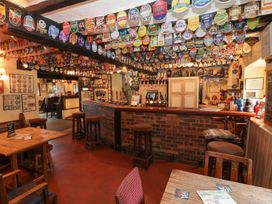 An interior view of a pub with a bar counter, bar stools, tables, chairs, and various beer labels and signs displayed on the ceiling and walls
