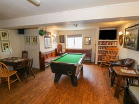 A room with a pool table in the center wooden bench seating a table with chairs a bookshelf a rocking chair and wall decorations at Heather in Graigfechan