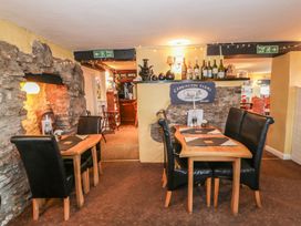 A dining area with wooden tables and black chairs near a stone wall and bar at Heather in Graigfechan