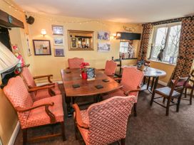 A dining room with wooden tables and upholstered chairs near a window with patterned curtains at Heather in Graigfechan