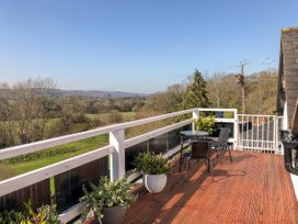 A balcony with potted plants a round table and two chairs overlooking trees and fields at Heather in Graigfechan