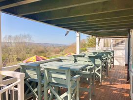 An outdoor covered terrace with wooden tables and chairs overlooking a landscape with trees at Heather in Graigfechan