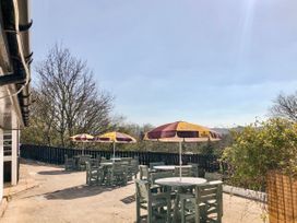 An outdoor patio with tables chairs and umbrellas next to a building and trees at Heather in Graigfechan