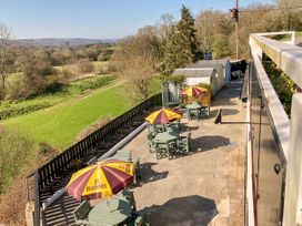 An outdoor patio with three tables and chairs under Bulmers umbrellas next to a grassy field at Heather in Graigfechan