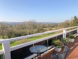 A balcony with glass tables chairs and potted plants overlooking trees and fields at Hillfort in Graigfechan