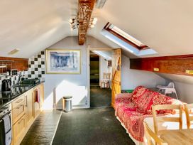 A kitchen and living area with wooden cabinets, a red patterned sofa, skylight, and a wooden dining table at Hillfort in Graigfechan