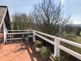 An outdoor balcony with wooden flooring two metal chairs a glass table and potted plants surrounded by trees at Hillfort in Graigfechan