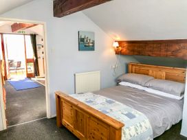A bedroom with a wooden bed and bedding and a doorway leading to a room with a glass door and outdoor seating at Hillfort in Graigfechan