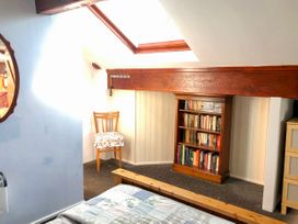 A bedroom with a wooden bed frame a bookshelf a wooden chair with a cushion and a skylight window at Hillfort in Graigfechan
