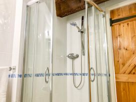A bathroom with a glass shower enclosure wooden door and white tiled walls with a blue mosaic tile border at Hillfort in Graigfechan