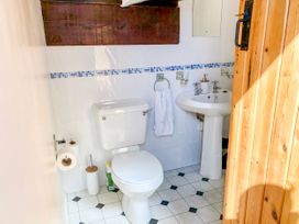 A bathroom with a toilet sink wooden door and tiled floor at Hillfort in Graigfechan
