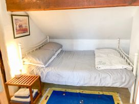 A small bedroom with a single bed a folded blanket a wooden side table with stacked towels a lamp a framed picture on the wall and a blue rug on the floor at Hillfort in Graigfechan