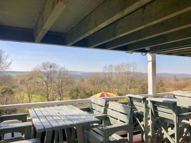 A balcony with wooden tables and chairs overlooking trees and hills at Hillfort in Graigfechan