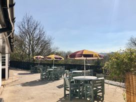 Outdoor seating area with tables chairs and umbrellas next to a building and trees at Hillfort in Graigfechan