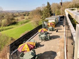 An outdoor seating area with green tables and chairs under yellow and brown umbrellas next to a wooden fence and green fields at Hillfort in Graigfechan