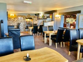 Interior of a dining area with wooden tables and black leather chairs with exposed stone wall and bar area