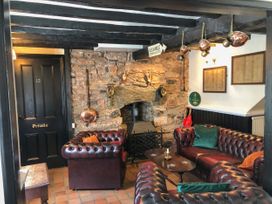 A sitting area with brown leather sofas around a wooden table and a stone fireplace at Hillfort in Graigfechan