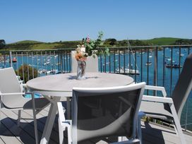 A balcony with a round table and chairs overlooking a harbor with boats and green hills at 34 The Salcombe in Salcombe