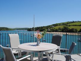 A round outdoor table with a vase of flowers and four chairs on a balcony overlooking a river with boats and green hills at 34 The Salcombe in Salcombe