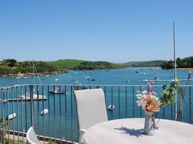 A balcony with a table, chairs, and a vase of flowers overlooking a river with boats and green hills at 34 The Salcombe in Salcombe