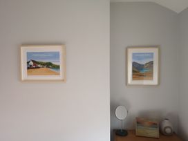 A wall with two framed landscape prints above a wooden surface holding a round mirror a painting and a vase at Y Bwthyn in Llanbedr
