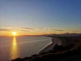 A sunset over a curved coastline with mountains in the distance at Y Bwthyn in Llanbedr
