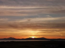 A sunset over mountains with a body of water and a dark land silhouette at Y Bwthyn in Llanbedr