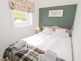 A bedroom with a double bed and two pillows with tree patterns a window with floral blinds and a bedside table with a lamp at Afallon in Penmachno