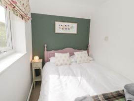 A bedroom with a double bed white bedding two patterned pillows green accent wall a bedside table with lamp and a window at Afallon in Penmachno