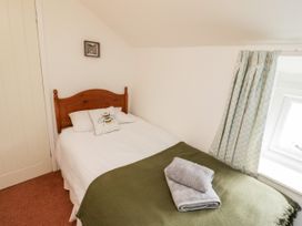 A bedroom with a wooden bed having white linens and a bee pillow with folded towels on an olive blanket at Afallon in Penmachno
