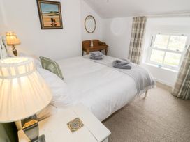 A bedroom with a bed with white linens and folded towels a bedside table with a lamp a small wooden desk with a mirror and a window with plaid curtains at Afallon in Penmachno