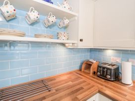 A kitchen corner with wooden countertops blue tiled backsplash white shelves holding polka dot cups plates and bowls a toaster paper towel holder and bread box at Afallon in Penmachno