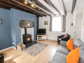 A living room with a grey sofa with orange cushions a black armchair a wood burning stove a television on a stand and exposed ceiling beams at Afallon in Penmachno