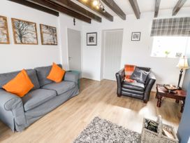 A living room with a gray sofa and orange pillows a black armchair with cushions a wooden side table with a lamp and bowl a window with plaid blind and framed pictures on white walls at Afallon in Penmachno