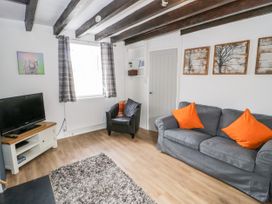 A living room with a gray sofa with orange pillows a black armchair a television on a white stand and artwork on white walls at Afallon in Penmachno