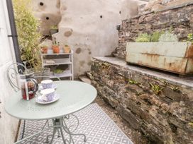 A small outdoor patio with a metal table and two chairs two teacups and a French press on the table potted plants on shelves and a stone wall with a planter box at Afallon Penmachno