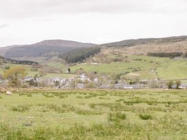 A rural landscape with grassy fields and scattered bushes and houses in the distance at Afallon in Penmachno