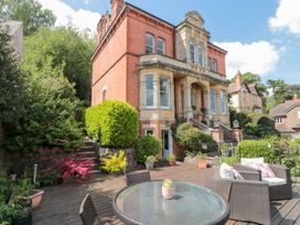 An outdoor patio with a glass round table and wicker chairs near a brick house with steps and greenery at The Hideaway in Malvern