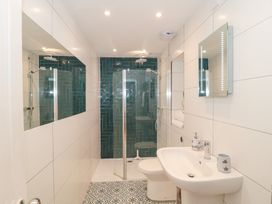 A bathroom with a sink, toilet, glass shower enclosure, patterned floor tiles and green tiles in the shower area at The Hideaway in Malvern