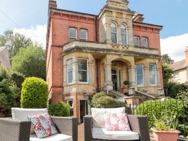 An outdoor seating area with two armchairs and pillows in front of a large brick house with stone architectural details and multiple windows