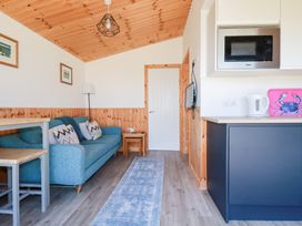 A living area with a blue sofa and cushions next to a wooden table and stools a kitchen counter with a microwave kettle and a pink tray with a crab design and a television mounted on the wall at 194 Atlantic Bays in Atlantic Bays Holiday Park near St Merryn