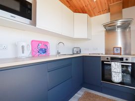 A kitchen with blue cabinets white upper cupboards a microwave a kettle a toaster an oven and a pink tray with a crab design at 194 Atlantic Bays in Atlantic Bays Holiday Park near St Merryn